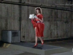 Rødhåret kvinne i røde sko med høye hæler knuller to svarte karer på sofaen
